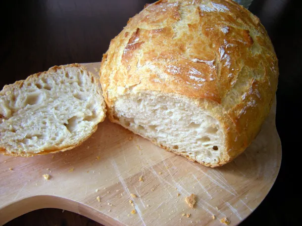 A warm analog film photograph of a round loaf of bread sliced open on a wooden cutting board, golden crust and pale interior, soft window light, visible film grain