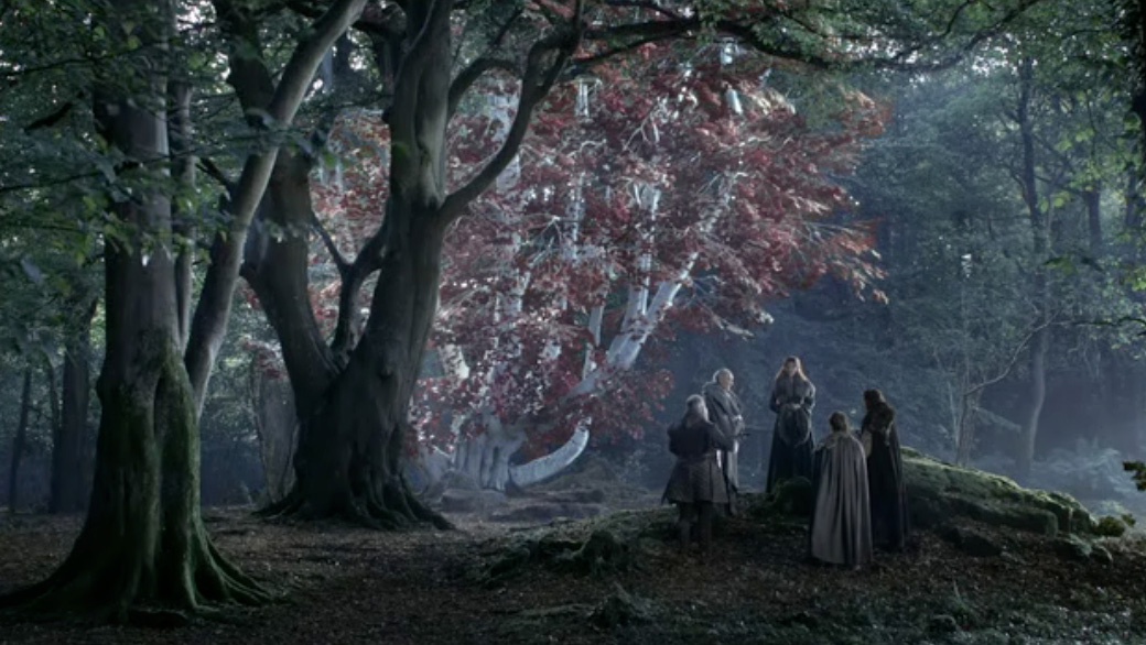A muted, warm analog film photograph of small silhouetted figures standing near a pale-barked tree with red leaves in a misty forest clearing, soft greens and amber tones, gentle film grain